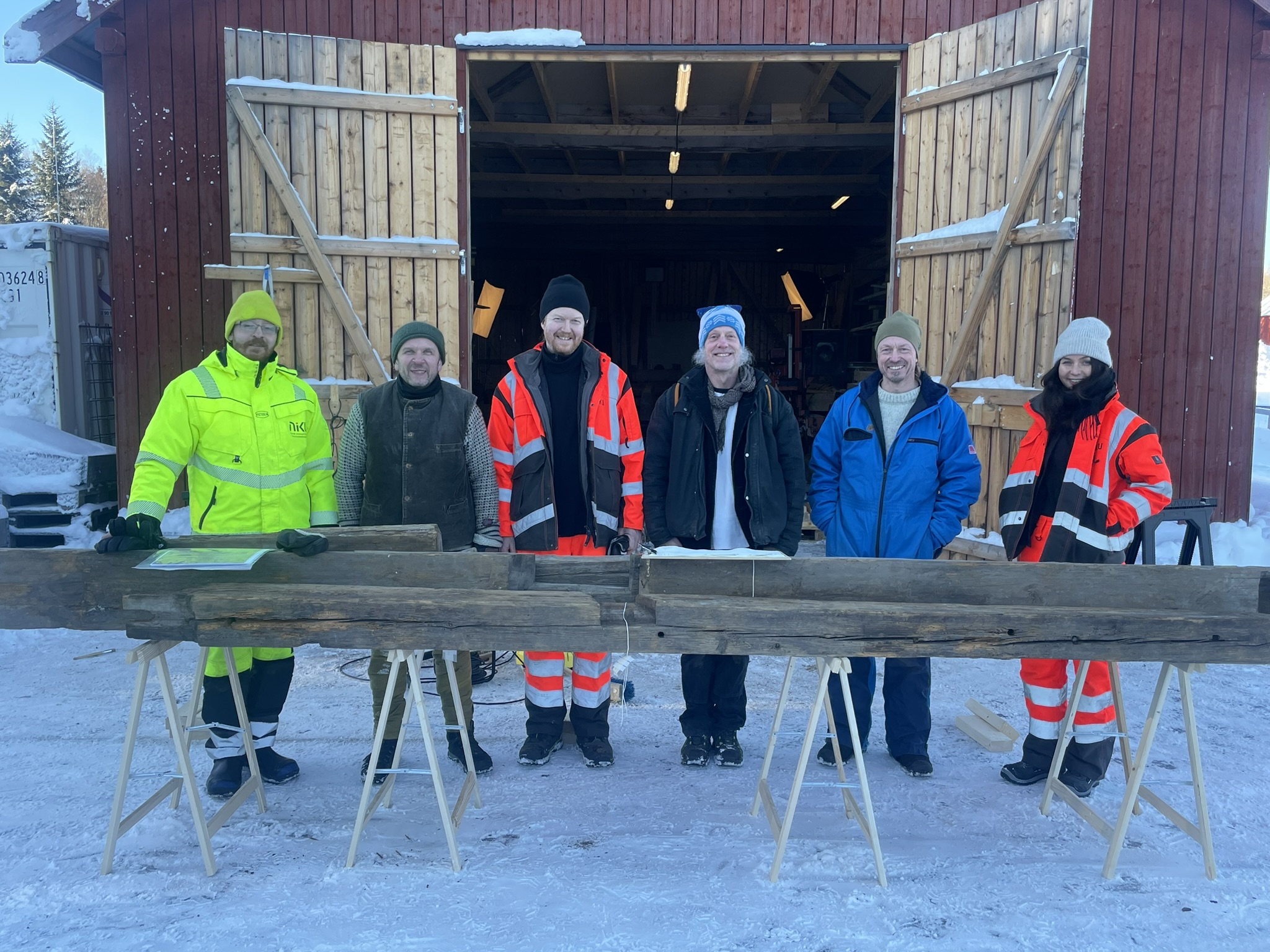 Seks mennesker står bak en laftet stokk og ser inn i kamera. De er teamet som jobber med å datere og dokumentere stokkene fra det opprinnelige Fløan kapell